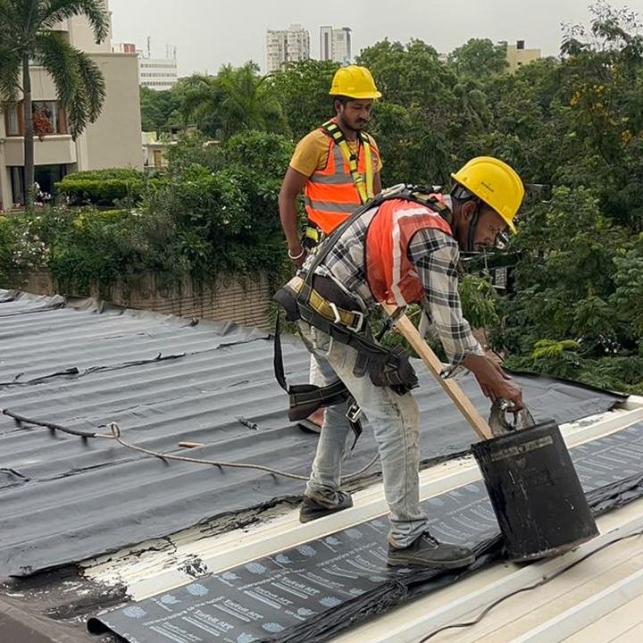 Applicators with a bitumen pot working beside a roof edge