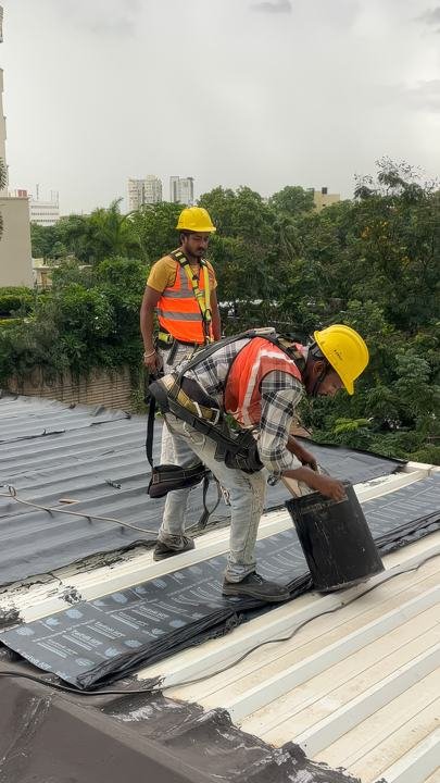 Applicators on a metal roof preparing sheet membrane